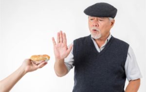 A senior man holding up his hand refusing to accept pizza bread as he knows it's not recommended to maintain good overall health and memory function