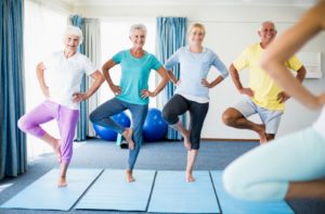 A group of 4 seniors participating in a yoga class, performing a balance exercise