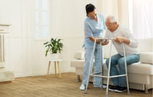 Female caregiver helping senior citizen stand up from couch