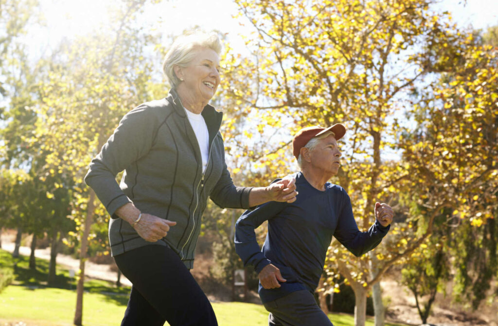 A senior woman and a senior man smiling while walking in a park.