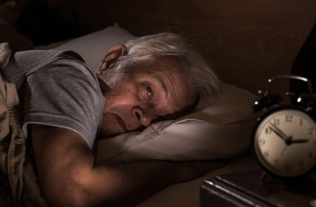 A senior man lying alone in a bed at night and unable to sleep.