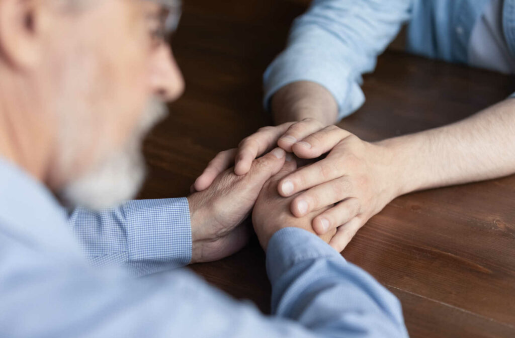 A son holding the hand of his older father, showing support, and talking to him about accepting help.