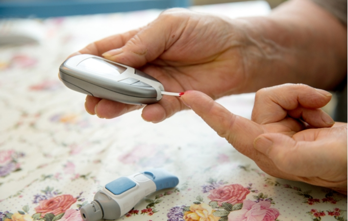 A close up of a seniors hands as they test their blood sugar due to diabetes.