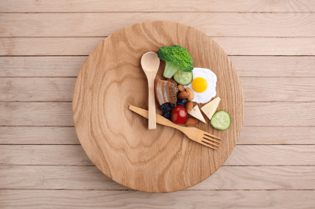 A wooden plate with a sunny side up egg and some greens with a spoon and fork to eat with.