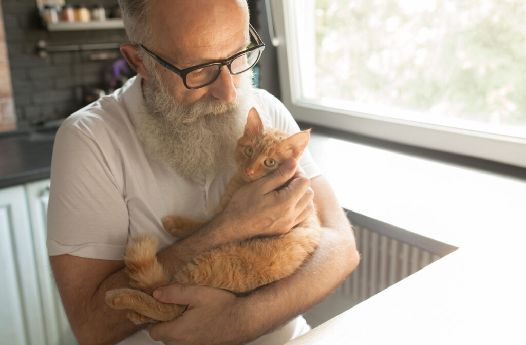A senior man with glasses holding a ginger cat at home