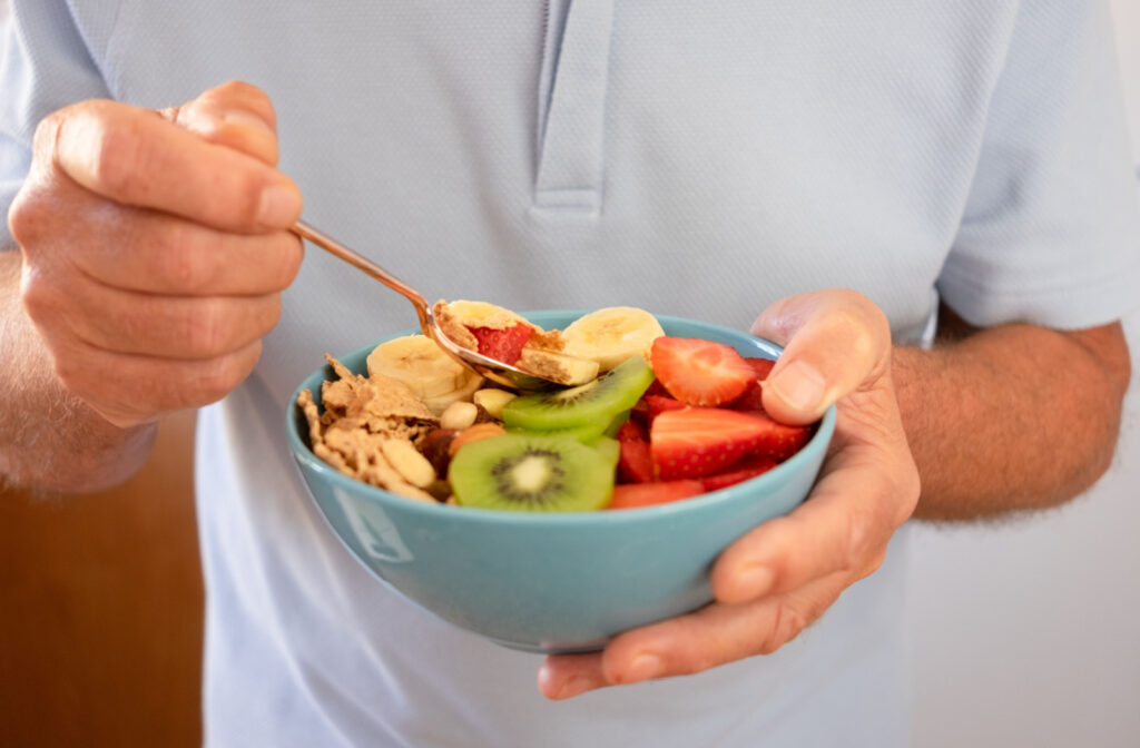 A senior man holding a bowl with granola, kiwi, bananas, and strawberries.