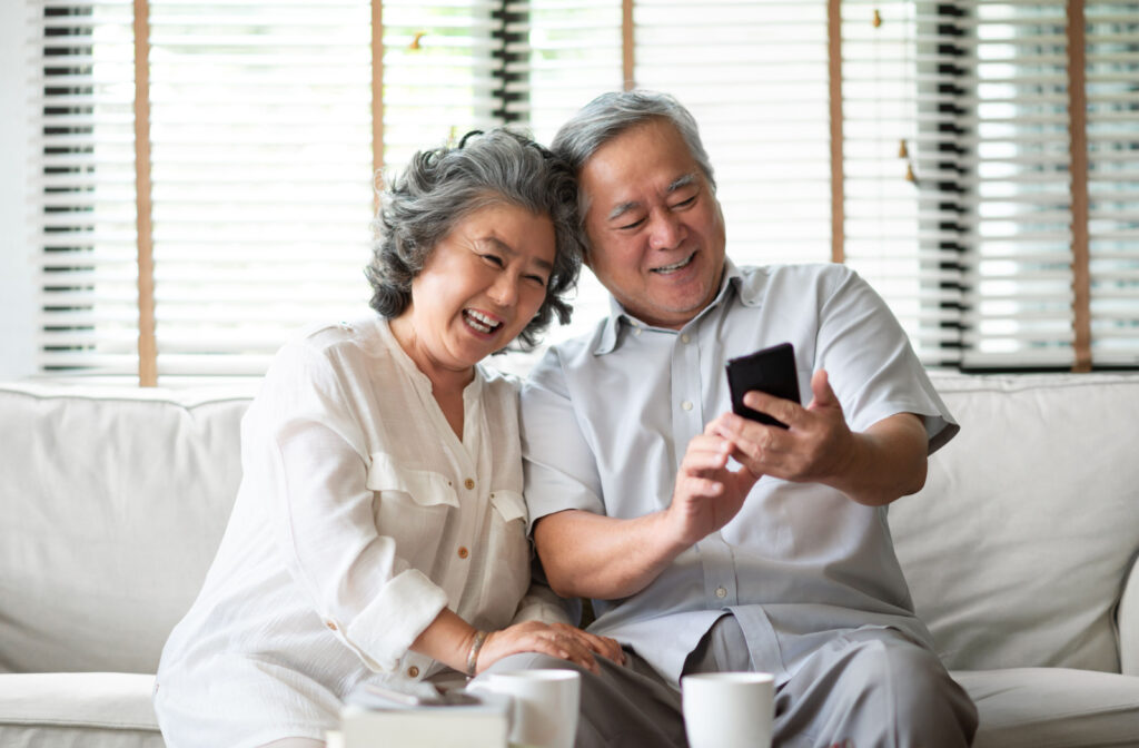 An older adult man and woman sitting on a couch doing a video call using a smartphone