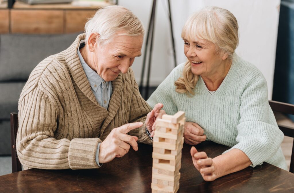 An older adult man and woman smiling while playing Jenga on a table