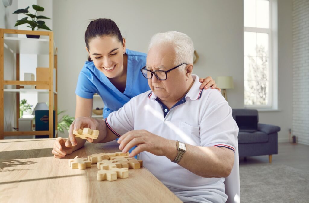 A female nurse smiling and helping an older adult man with a board game