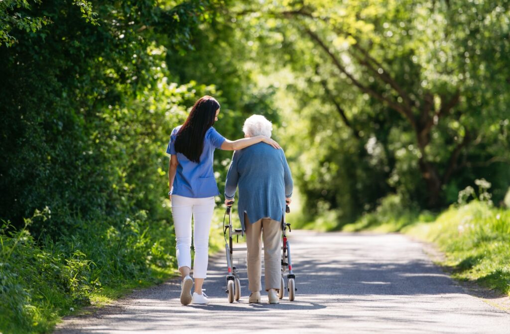 A senior & their caregiver taking a walk in the park on a sunny day.