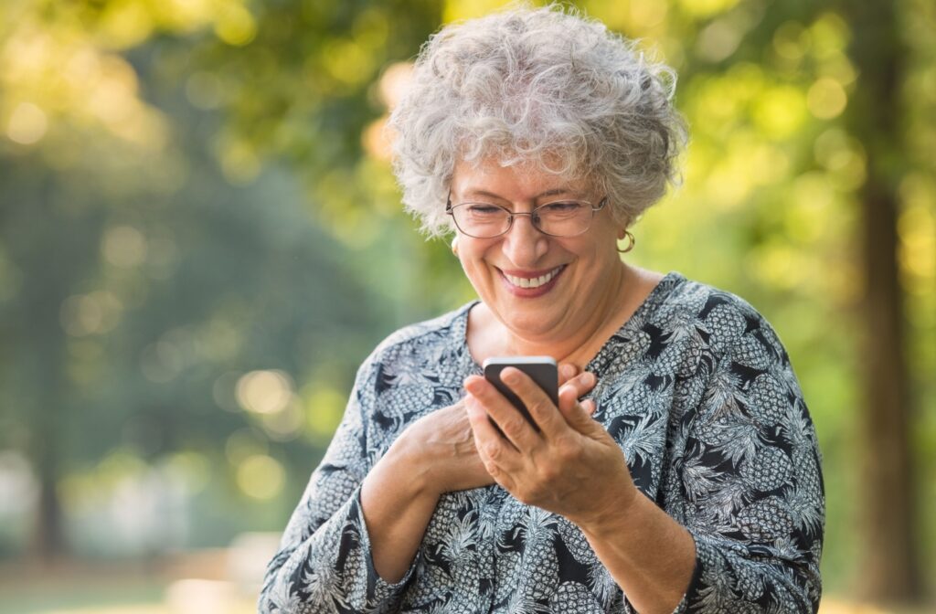 An older adult smiling while on a walk in the park as they check their new phone.