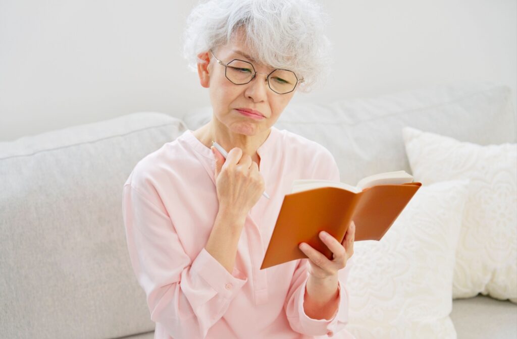 Older adult with short white hair and glasses thoughtfully reading a notebook while seated on a light-colored couch