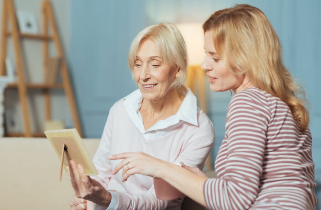A senior looks thoughtfully at a photo in memory care while their child points at it, reminding their parent of the people within the photo.