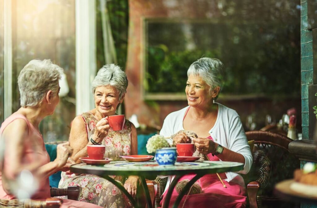 A group of senior friends enjoy lunch and coffee together while chatting and knitting.