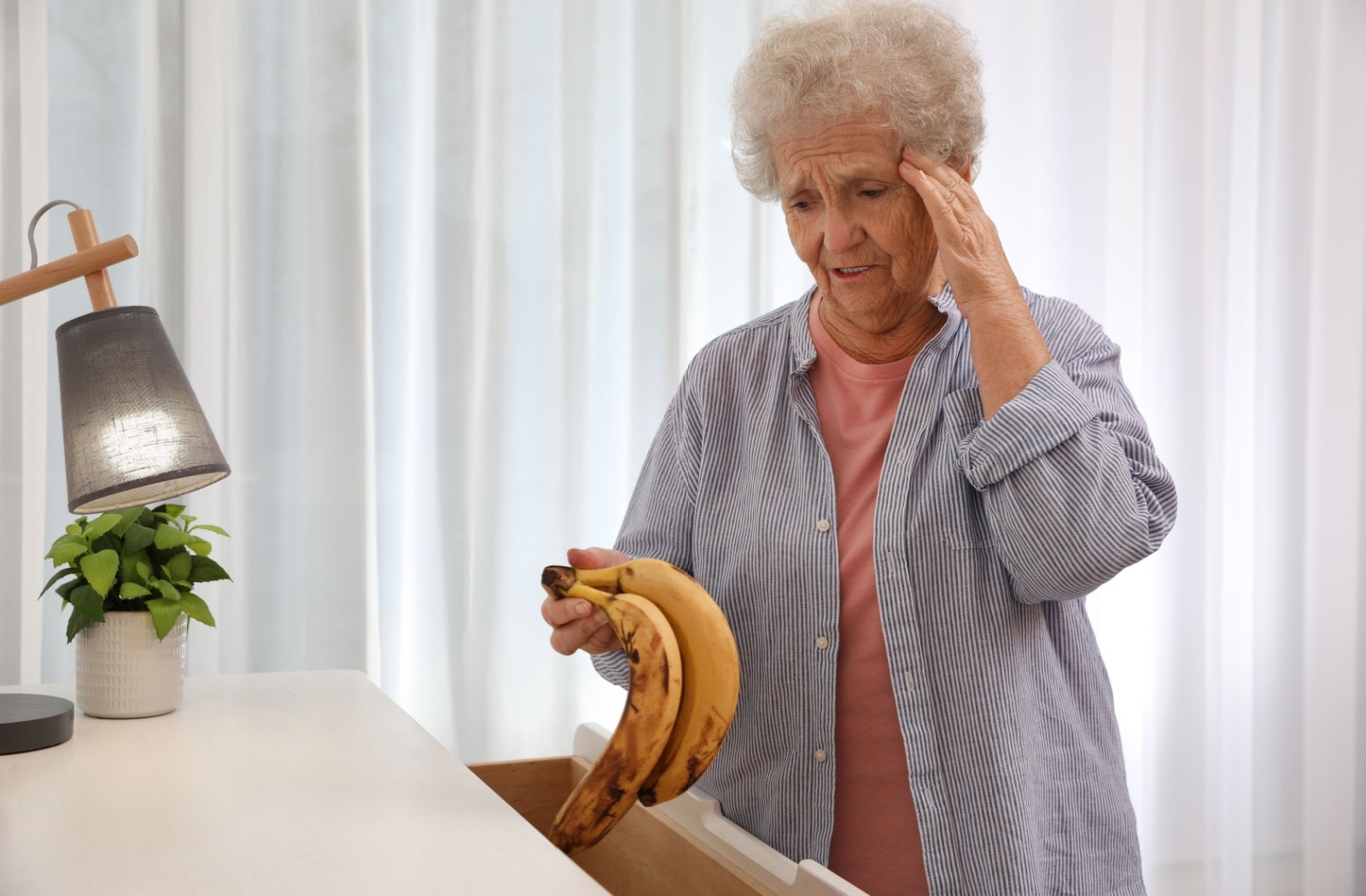 A senior holds bananas, wondering how they got into a chest of drawers.